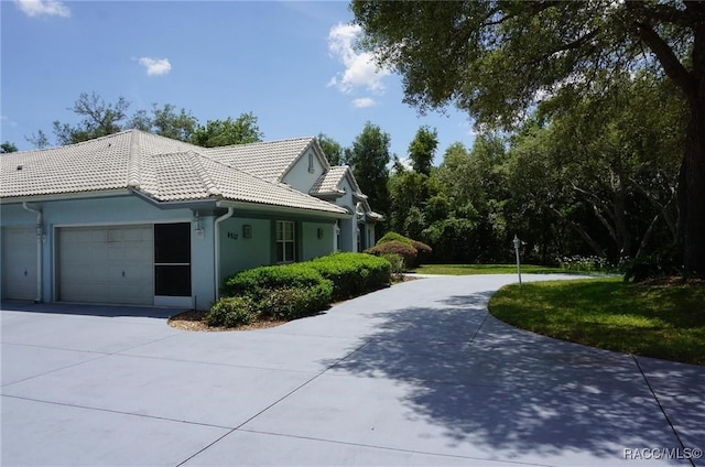 view of side of property featuring driveway, stucco siding, a tiled roof, and a garage