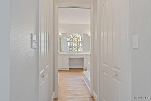 corridor featuring light wood-style flooring, a desk, and a textured wall