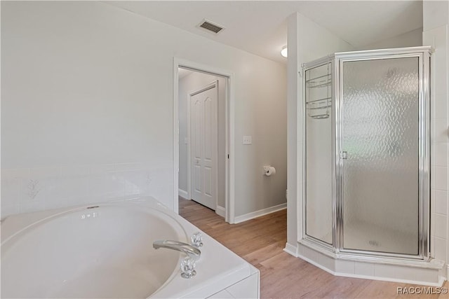 bathroom with a stall shower, a garden tub, wood finished floors, and baseboards