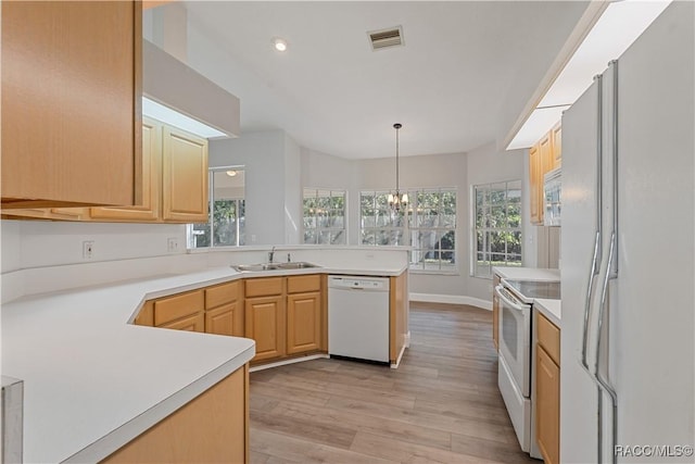 kitchen featuring white appliances, a sink, a peninsula, light wood-style floors, and healthy amount of natural light