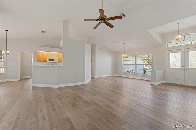 unfurnished living room with a chandelier, lofted ceiling, a ceiling fan, light wood-style floors, and baseboards