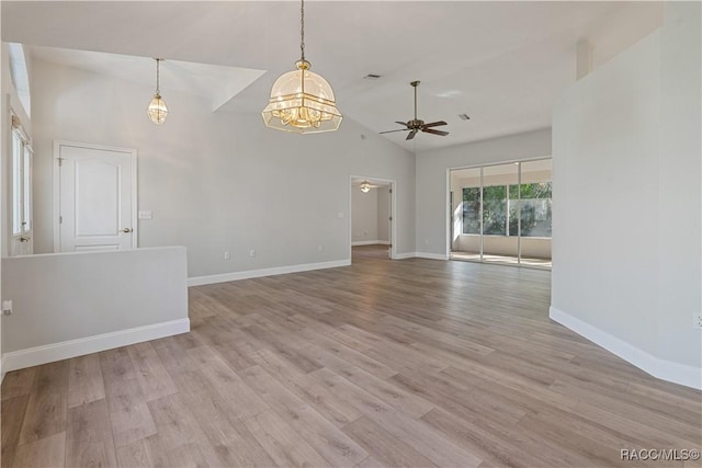 empty room with ceiling fan, a chandelier, high vaulted ceiling, light wood-style flooring, and baseboards