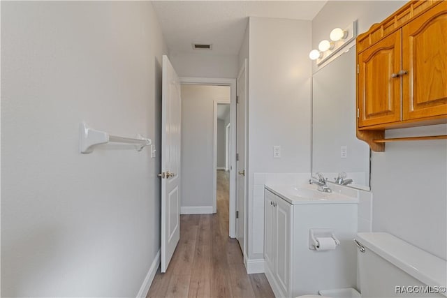 bathroom featuring toilet, vanity, wood finished floors, and baseboards