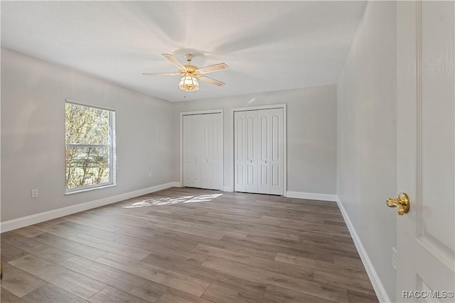 unfurnished bedroom with two closets, baseboards, wood finished floors, and a ceiling fan