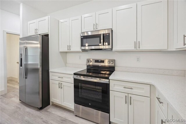 7820 N Sarazen Dr, Citrus Springs, FL 34434 - kitchen featuring appliances with stainless steel finishes, light wood finished floors, white cabinetry, and light stone countertops
