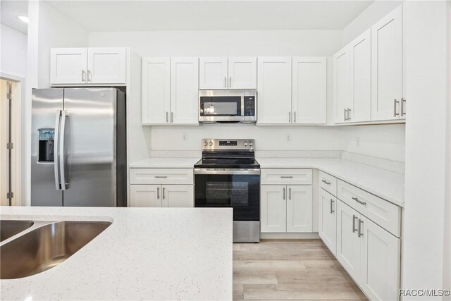 7820 N Sarazen Dr, Citrus Springs, FL 34434 - kitchen with appliances with stainless steel finishes, white cabinetry, light wood-style flooring, and light stone counters