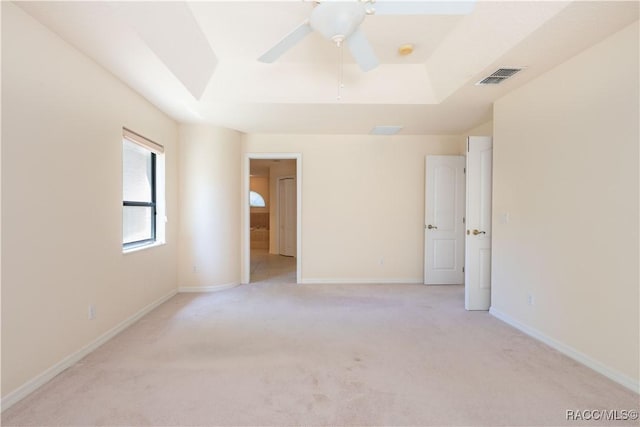 unfurnished bedroom featuring visible vents, baseboards, a tray ceiling, and light colored carpet
