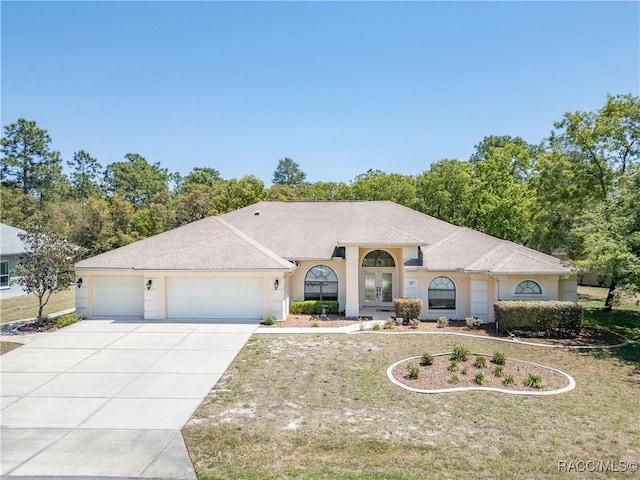 view of front facade with stucco siding, an attached garage, driveway, french doors, and a front yard
