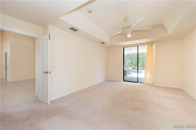 spare room featuring visible vents, baseboards, a ceiling fan, a tray ceiling, and light colored carpet