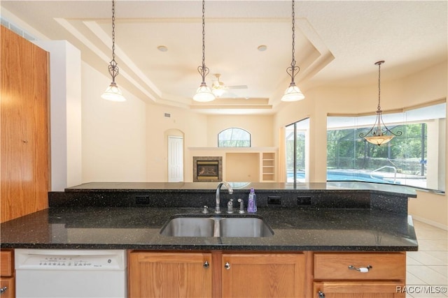 kitchen with dark stone countertops, pendant lighting, a raised ceiling, dishwasher, and a sink