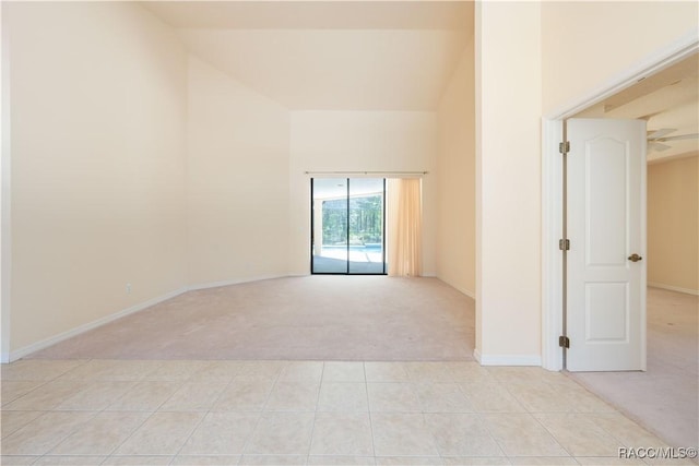 empty room with baseboards, high vaulted ceiling, light carpet, and light tile patterned floors