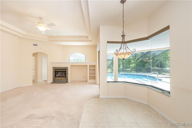 unfurnished living room with visible vents, a tray ceiling, ceiling fan, arched walkways, and a tile fireplace