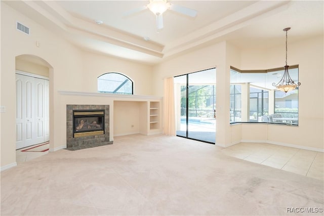 unfurnished living room featuring ceiling fan, arched walkways, visible vents, carpet flooring, and a tiled fireplace