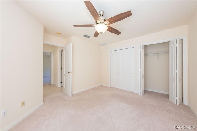 unfurnished bedroom featuring baseboards, a ceiling fan, visible vents, multiple closets, and light colored carpet