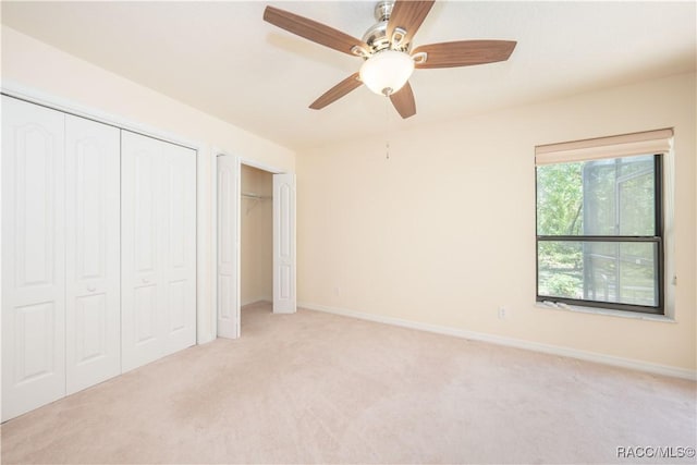 unfurnished bedroom with multiple closets, baseboards, ceiling fan, and light carpet