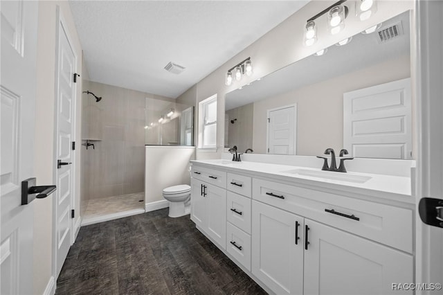 bathroom featuring a tile shower, hardwood / wood-style flooring, vanity, toilet, and a textured ceiling