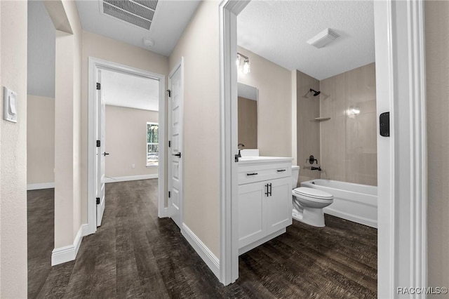 full bathroom with vanity, wood-type flooring, a textured ceiling, tiled shower / bath, and toilet