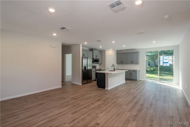 kitchen featuring gray cabinetry, sink, light hardwood / wood-style flooring, an island with sink, and stainless steel appliances