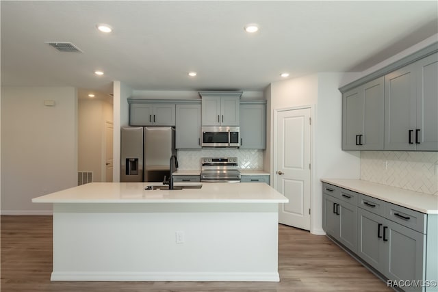 kitchen featuring sink, stainless steel appliances, light hardwood / wood-style flooring, gray cabinets, and a center island with sink