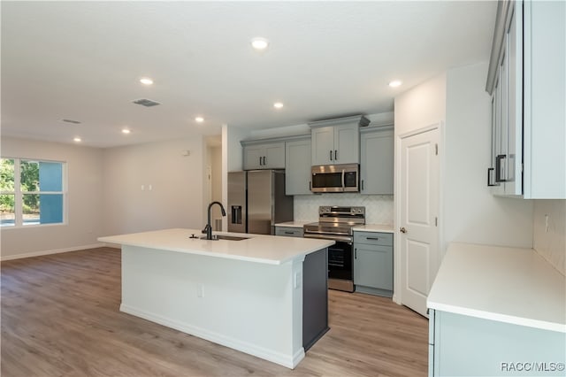 kitchen with sink, stainless steel appliances, light hardwood / wood-style flooring, an island with sink, and gray cabinets