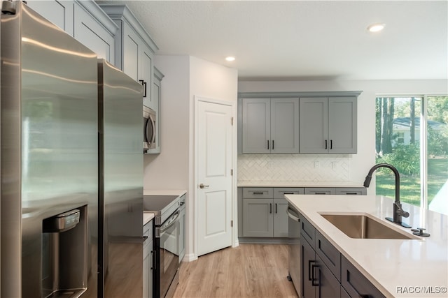 kitchen featuring light wood-type flooring, tasteful backsplash, stainless steel appliances, sink, and gray cabinets