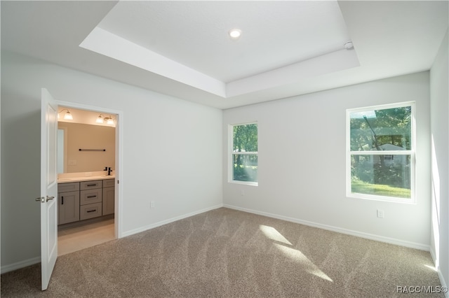 unfurnished bedroom with connected bathroom, a raised ceiling, and multiple windows