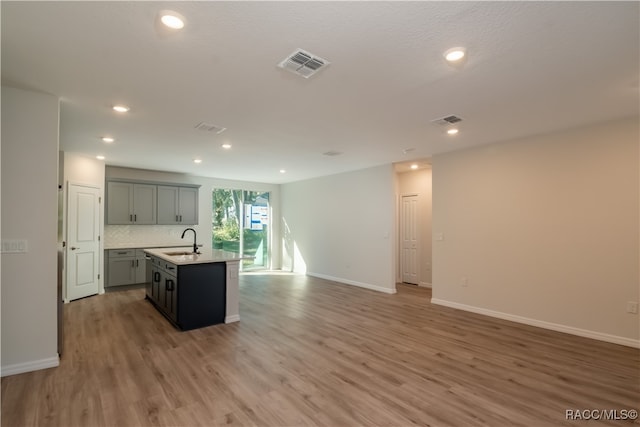 kitchen with sink, gray cabinets, light wood-type flooring, an island with sink, and tasteful backsplash