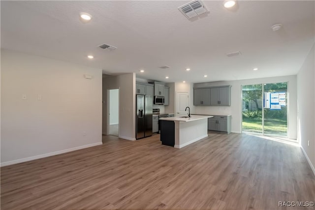 kitchen with gray cabinets, appliances with stainless steel finishes, sink, a kitchen island with sink, and light hardwood / wood-style floors