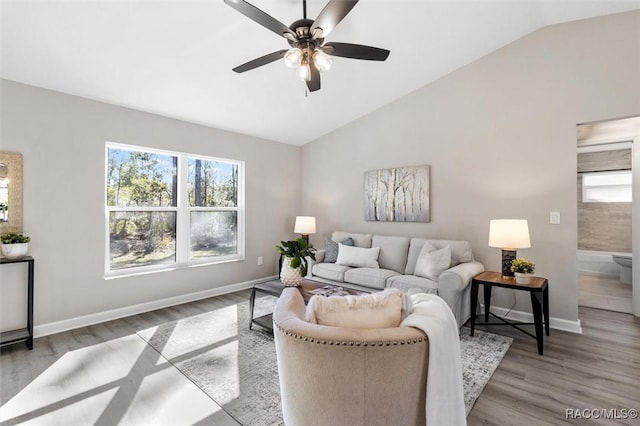 living area with ceiling fan, light wood-style flooring, baseboards, and vaulted ceiling