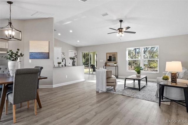 living room featuring baseboards, visible vents, lofted ceiling, wood finished floors, and recessed lighting