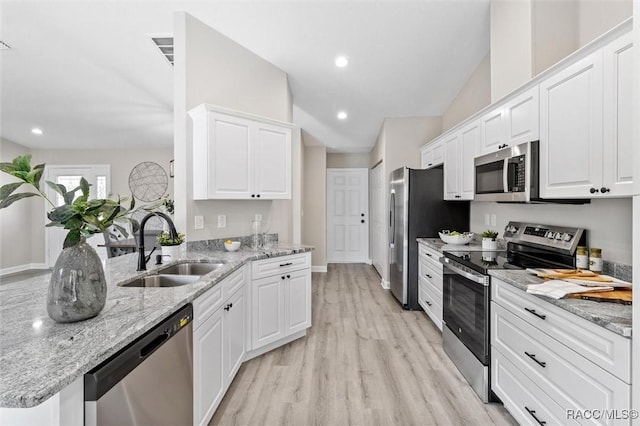 kitchen with light wood-style flooring, appliances with stainless steel finishes, light stone counters, white cabinetry, and a sink