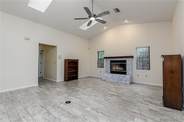 unfurnished living room featuring light wood-type flooring, a skylight, a brick fireplace, ceiling fan, and high vaulted ceiling