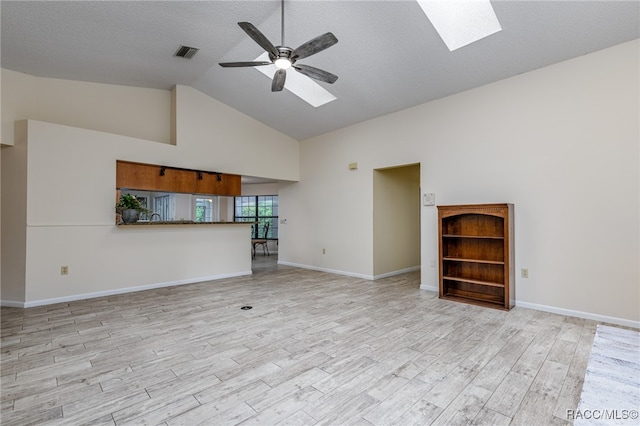 unfurnished living room featuring high vaulted ceiling, a skylight, ceiling fan, a textured ceiling, and light hardwood / wood-style floors