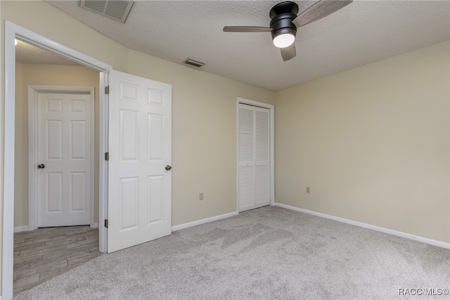 unfurnished bedroom with a textured ceiling, a closet, light colored carpet, and ceiling fan