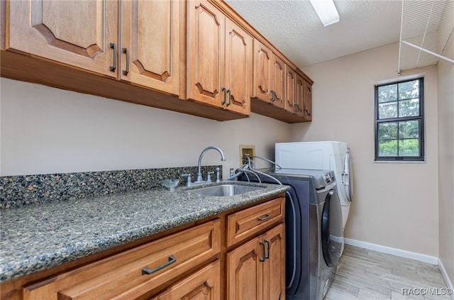 laundry room featuring sink, cabinets, a textured ceiling, washer and dryer, and light wood-type flooring