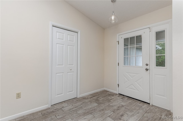 entryway with a textured ceiling, lofted ceiling, and light wood-type flooring