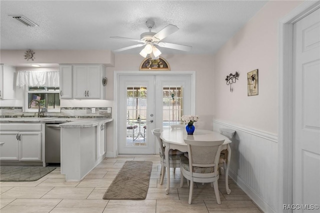 kitchen with french doors, stainless steel dishwasher, a textured ceiling, and white cabinets