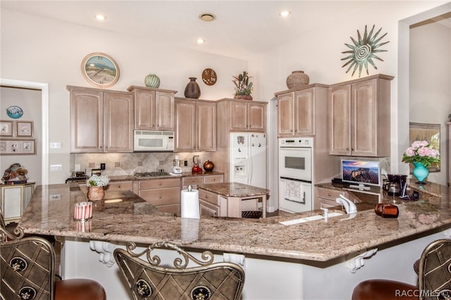 kitchen featuring white appliances, sink, light stone countertops, kitchen peninsula, and a breakfast bar area