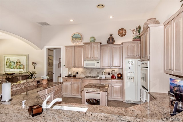 kitchen with light stone countertops, kitchen peninsula, white appliances, sink, and a center island