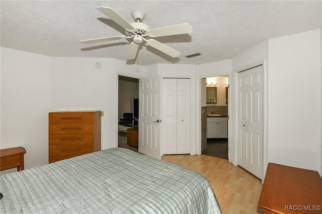 bedroom with ceiling fan, light hardwood / wood-style floors, a textured ceiling, and ensuite bathroom