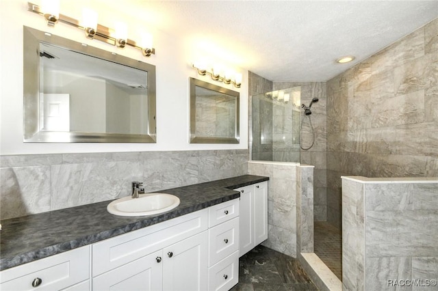 bathroom with a textured ceiling, a tile shower, vanity, and tile walls