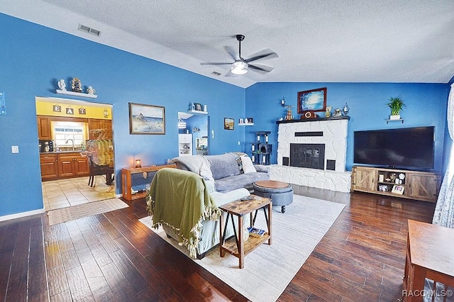 living room featuring a stone fireplace, hardwood / wood-style floors, lofted ceiling, ceiling fan, and a textured ceiling