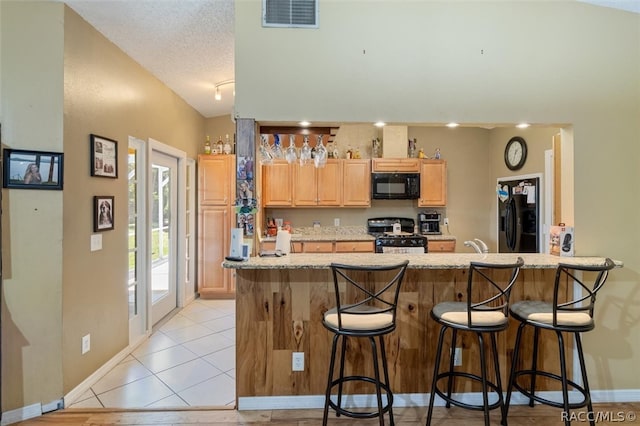 kitchen featuring black appliances, vaulted ceiling, a textured ceiling, kitchen peninsula, and a breakfast bar area