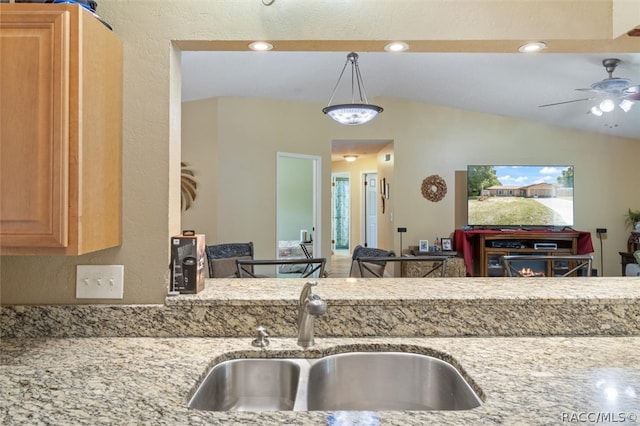 kitchen with ceiling fan, sink, light stone countertops, vaulted ceiling, and decorative light fixtures