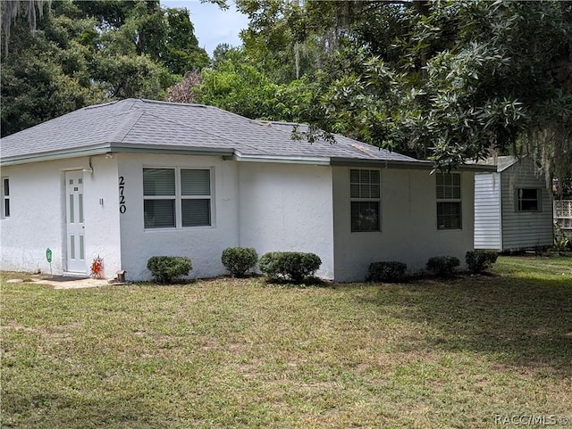 view of property exterior featuring a shingled roof, a lawn, and stucco siding