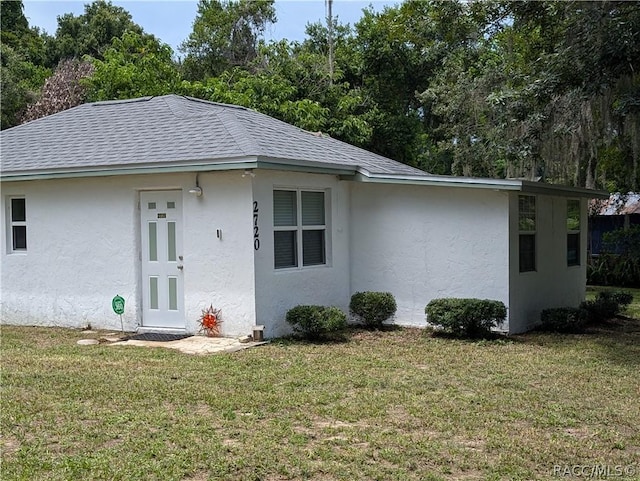 exterior space with a front yard, roof with shingles, and stucco siding