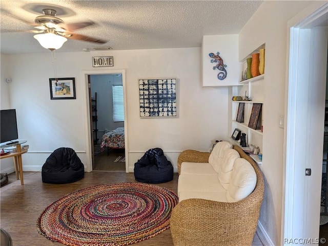 sitting room featuring a textured ceiling, wood finished floors, a ceiling fan, and baseboards