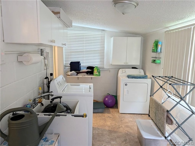 clothes washing area featuring concrete block wall, cabinet space, a textured ceiling, and washing machine and clothes dryer