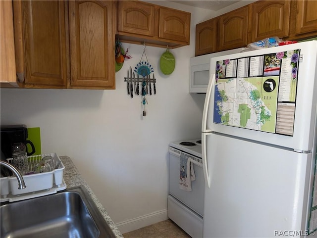 kitchen with white appliances, a sink, baseboards, light countertops, and brown cabinetry