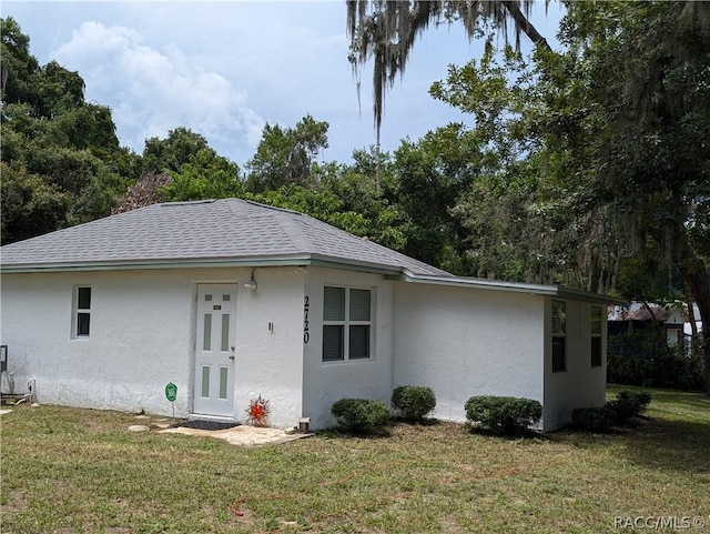 view of front of house with a shingled roof, a front lawn, and stucco siding